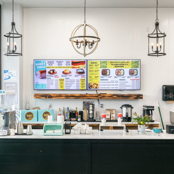 A clean counter at Budda's Hawaiian Bakery & Grill with digital menu boards displaying Hawaiian dishes.