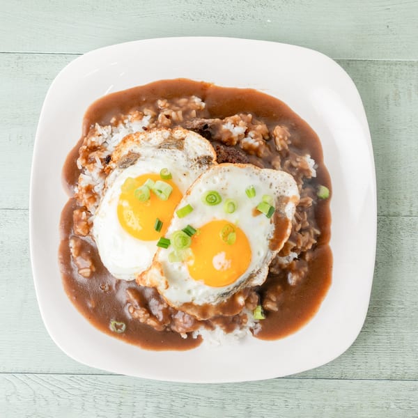Hawaiian Loco Moco with two fried eggs, rice, hamburger patty, and brown gravy, garnished with green onions.
