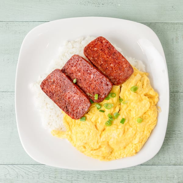 A Hawaiian breakfast plate with white rice, scrambled eggs, and three slices of Spam, garnished with green onions.