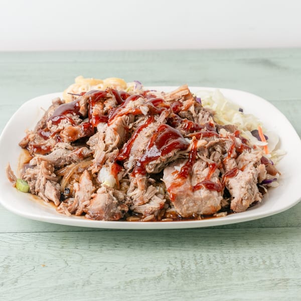 A white plate of Budda's Hawaiian pulled pork with barbecue sauce, macaroni salad, and coleslaw.