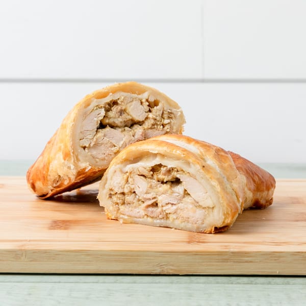 Two halves of a golden-brown chicken pastry, revealing a savory chicken filling on a wooden board.