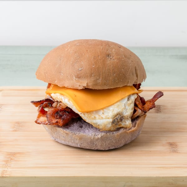 Hawaiian breakfast sandwich with bacon, egg, and cheese on a purple bun, on a wooden board.