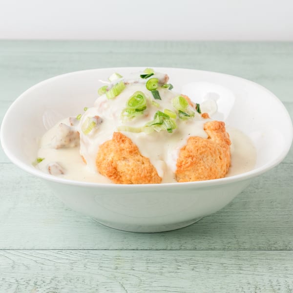 Hawaiian biscuits and gravy, topped with green onions, served in a white bowl.