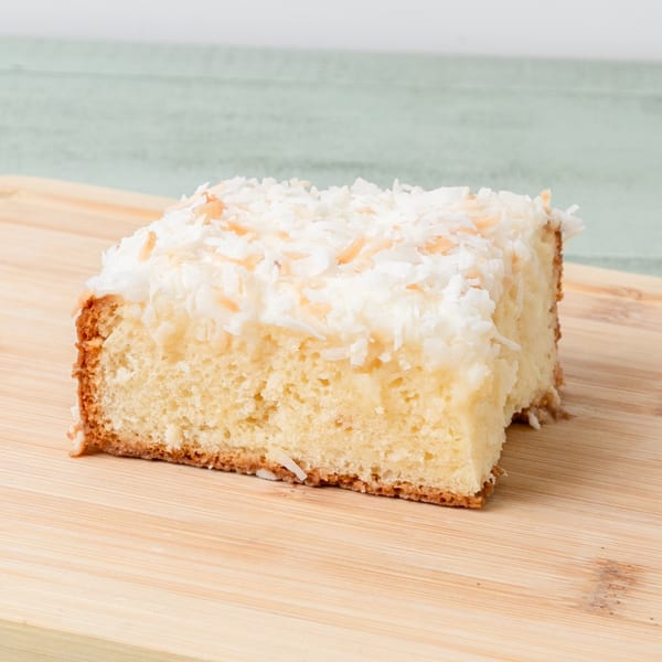 A slice of Budda's Hawaiian Bakery & Grill coconut cake with white frosting and toasted coconut flakes.